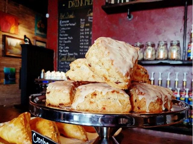 Glazed scones stacked on metal stand, with chalkboard drinks menu and syrup bottles.