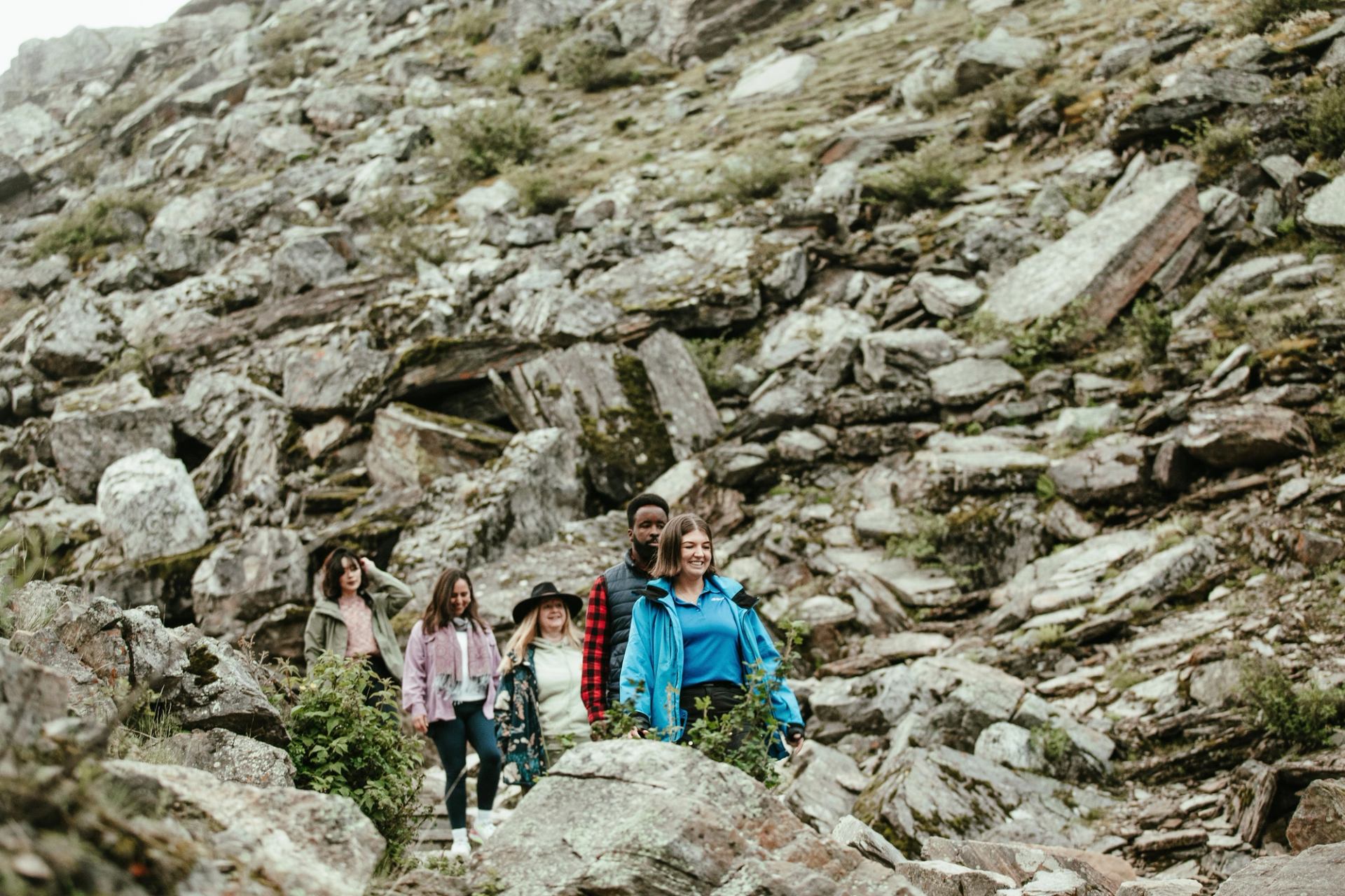 Group of hikers walking along rocky mountain trail surrounded by boulders and sparse vegetation.