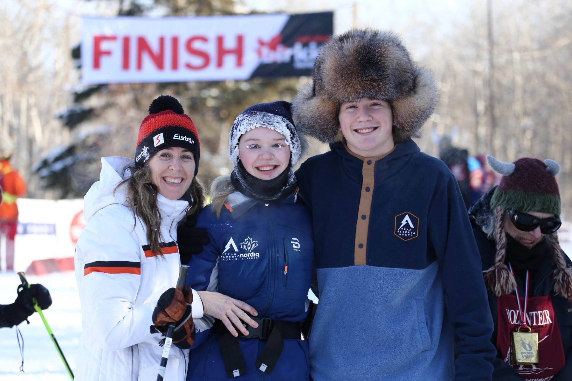 Two women and man smiling in front of the finish line of the Canadian Birkie.