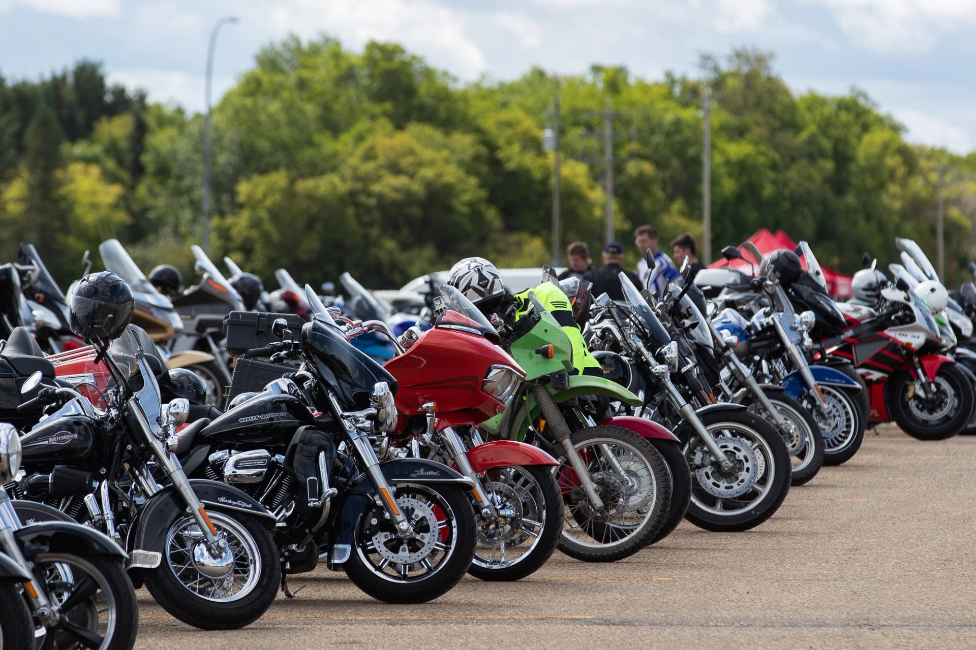 Close row of motorcycles lined up with trees and sky in the background.