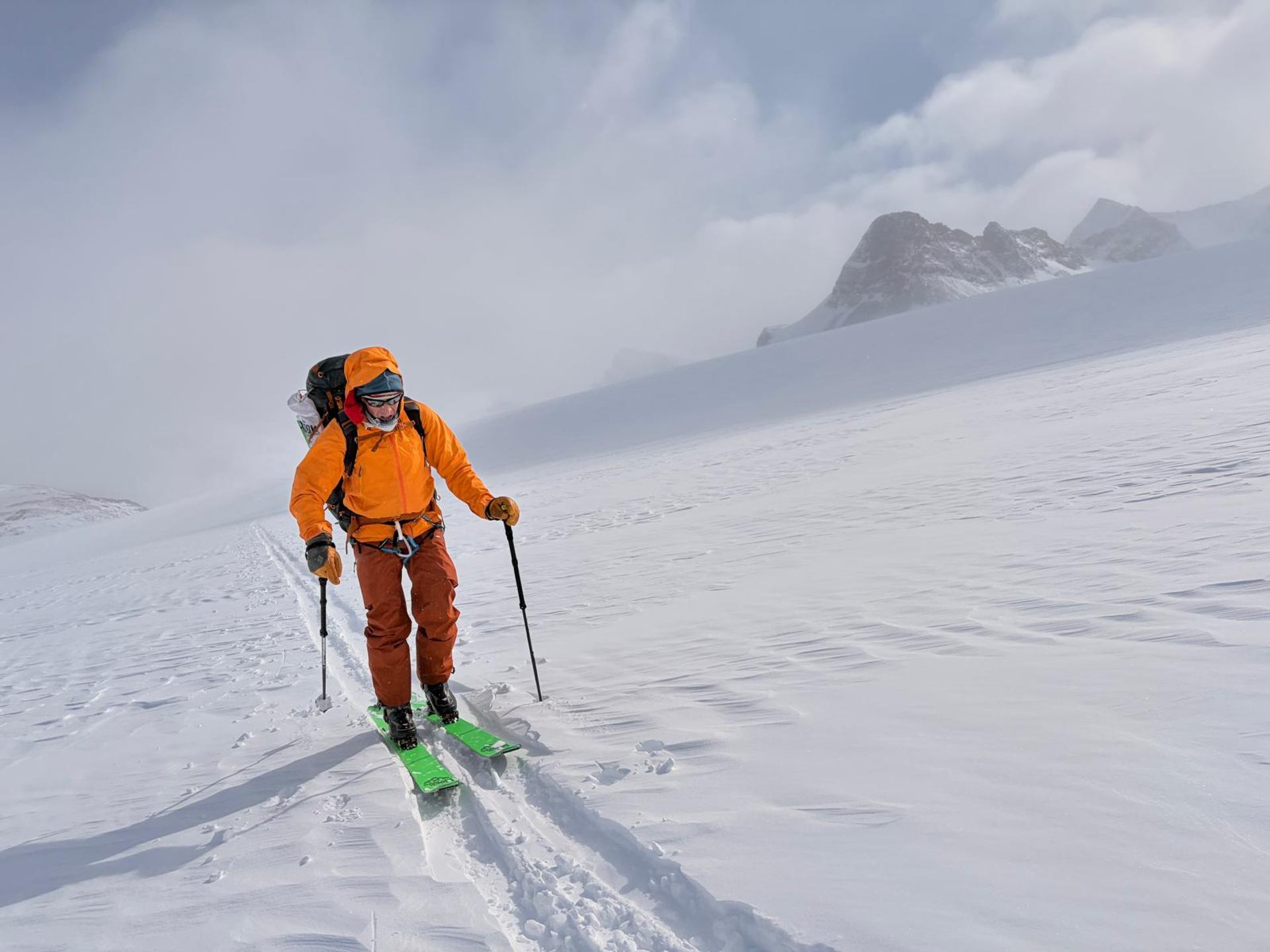 Skier touring across a wide snow-covered alpine slope with mountains rising in the distance.