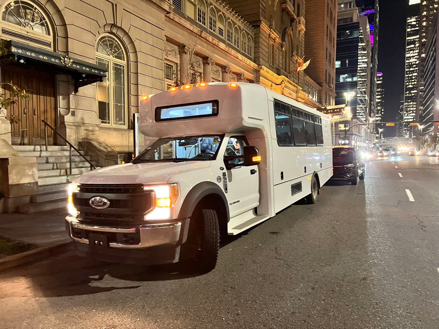 White shuttle bus parked beside an ornate stone building on a lit city street.