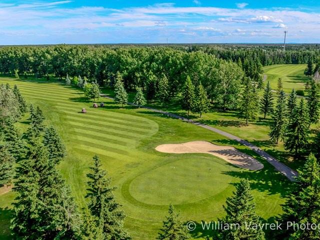 Aerial view of a green golf course surrounded by trees under a blue sky.