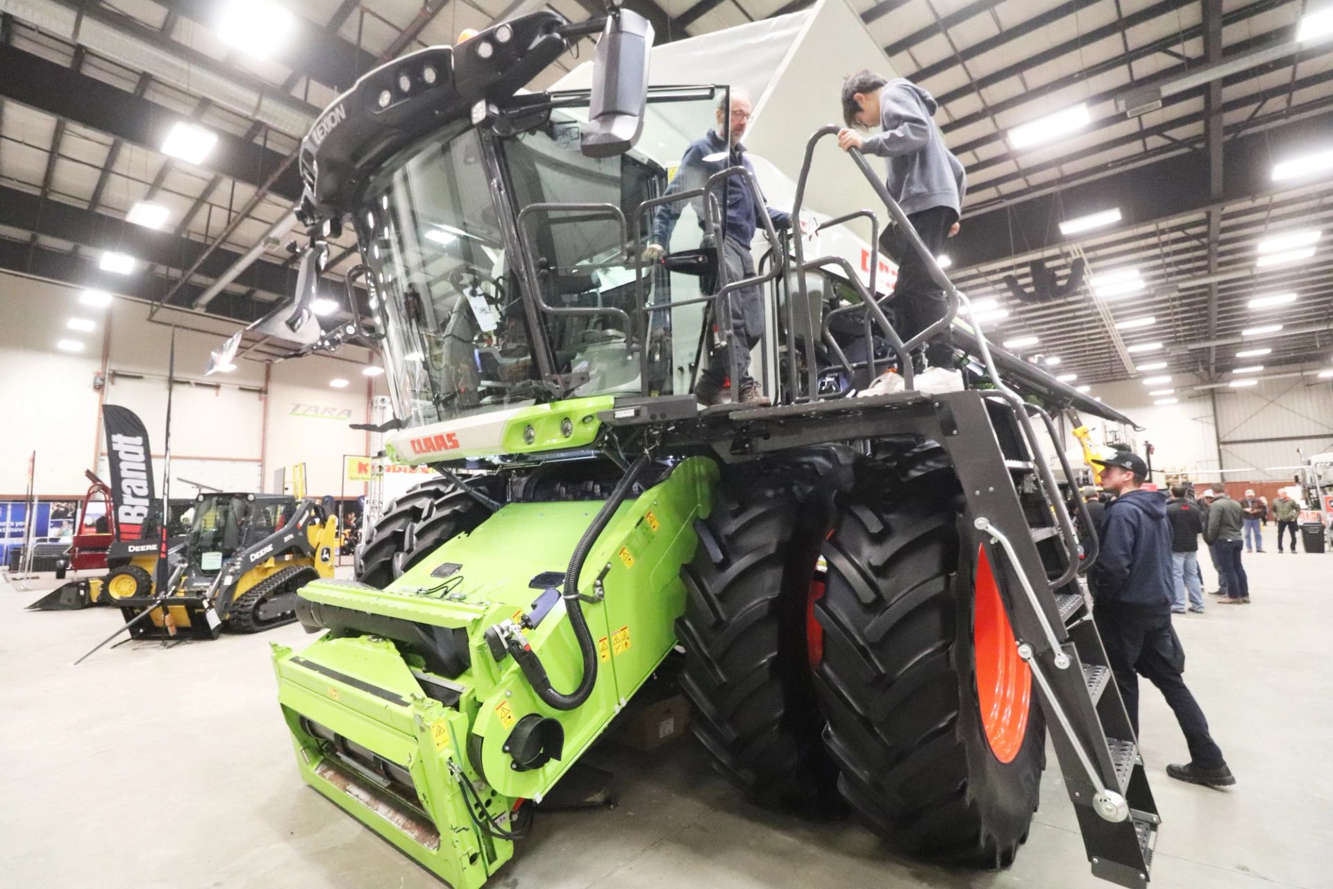 Large green combine harvester on display indoors with visitors viewing equipment.