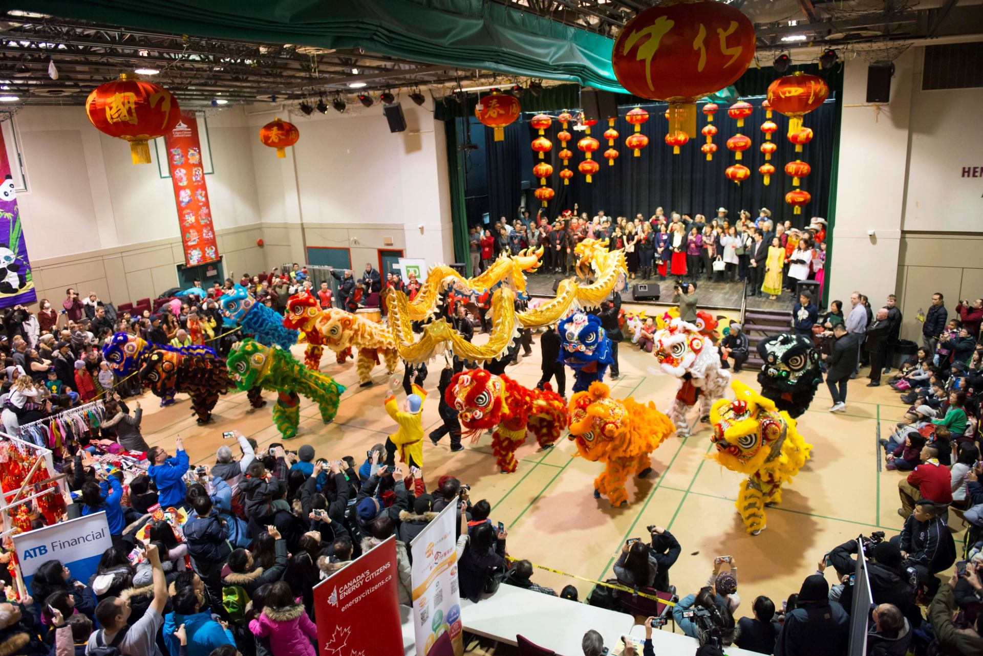 Indoor Chinese New Year event with colorful dragon dances and red lanterns above the stage.