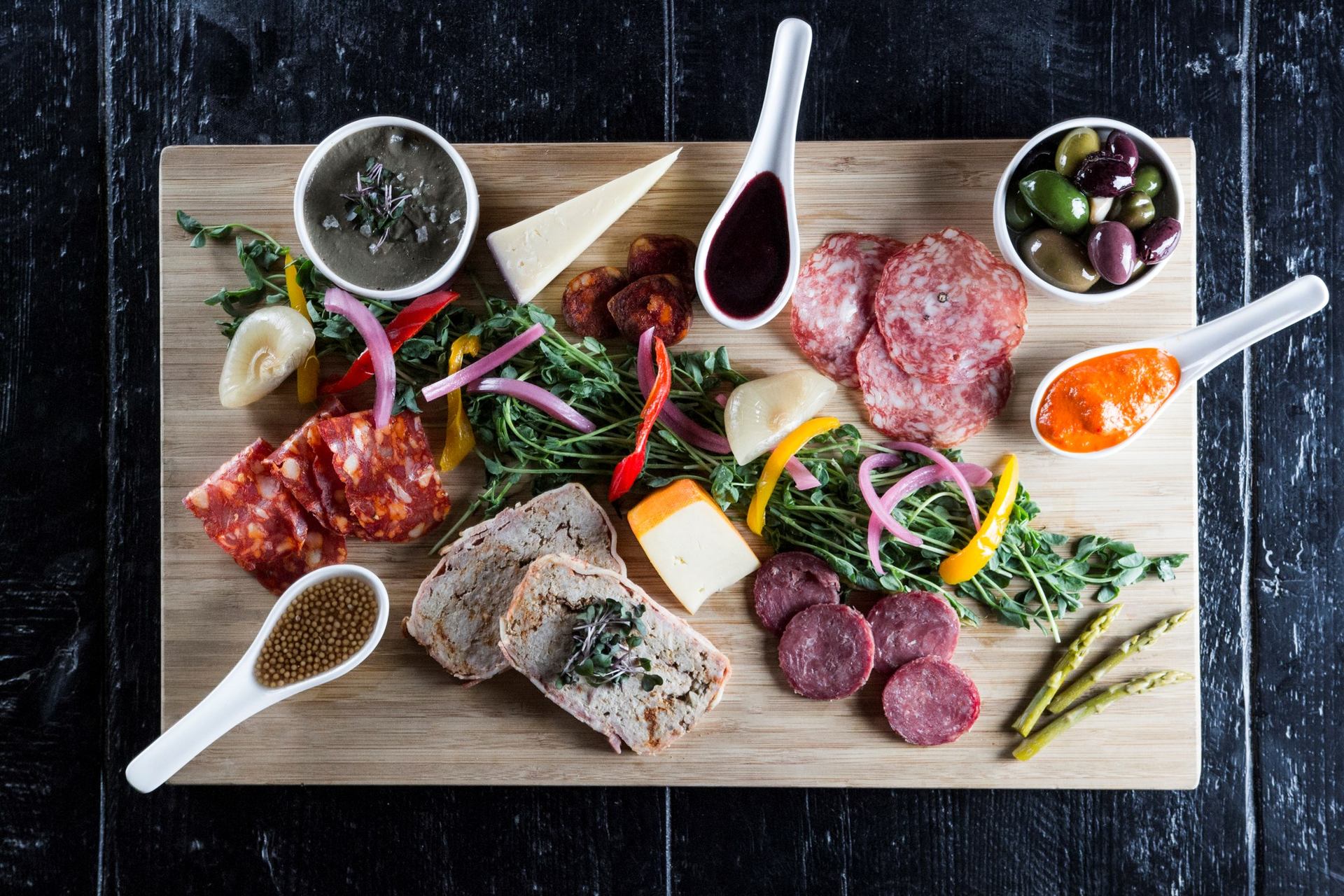 Charcuterie board with meats, cheeses, bread, veggies, and dipping sauces.
