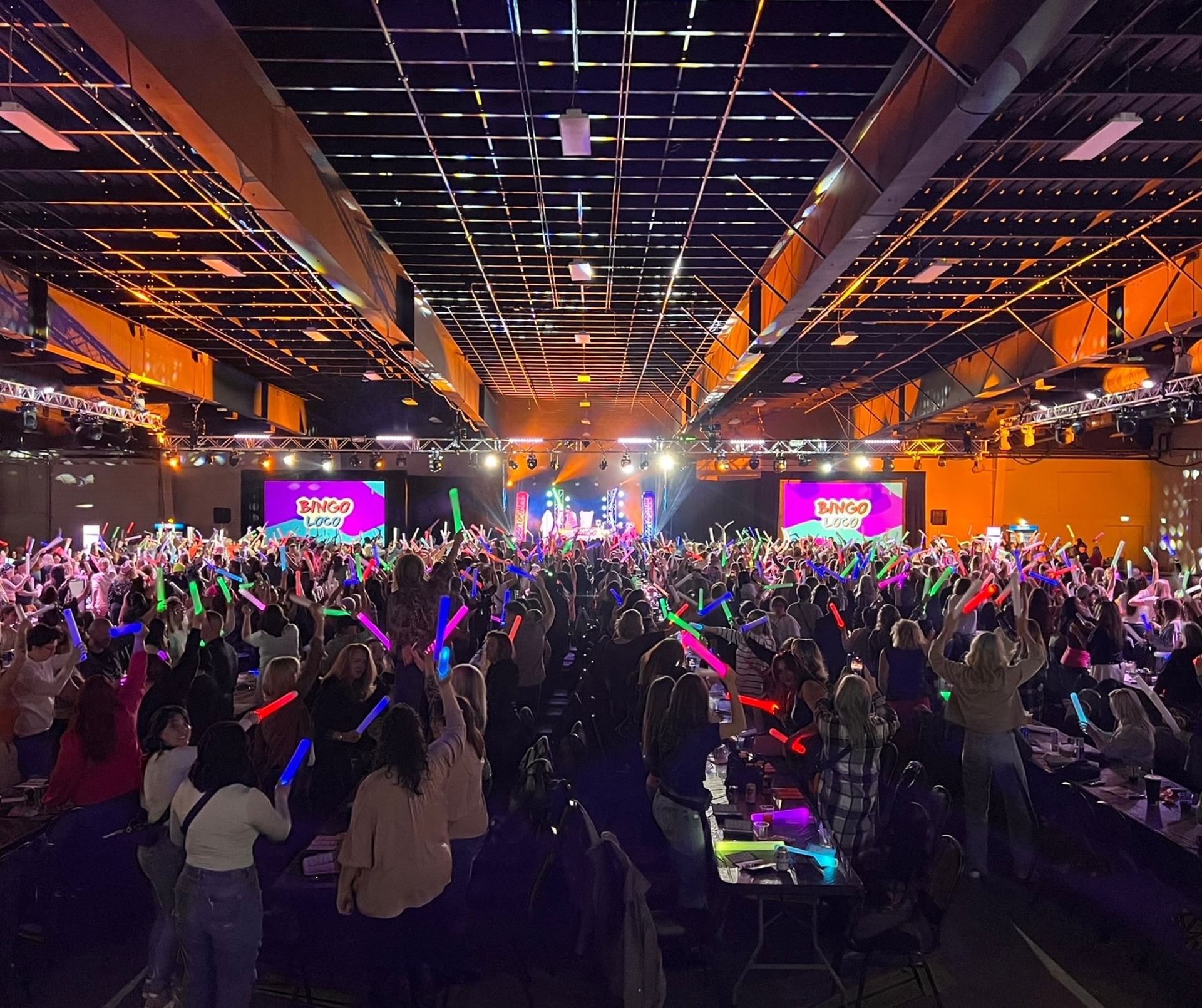 Crowd at a lively Bingo event with bright lights and 'Bingo' on large screens.
