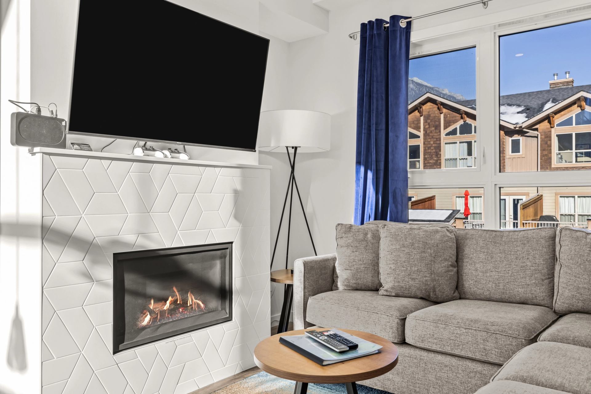 Living room with grey sectional, lit fireplace, wall-mounted TV and mountain-facing windows.