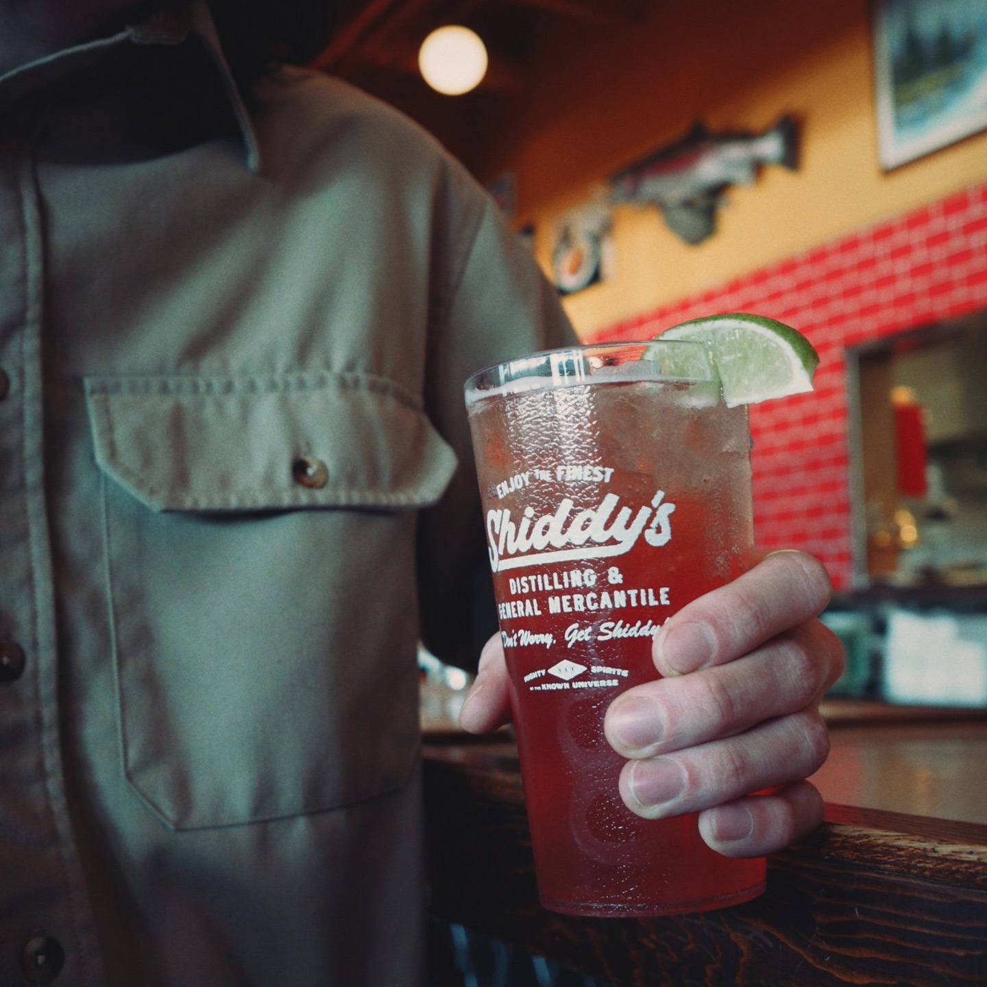 Hand holding a Shiddy's branded cocktail garnished with lime inside the restaurant.