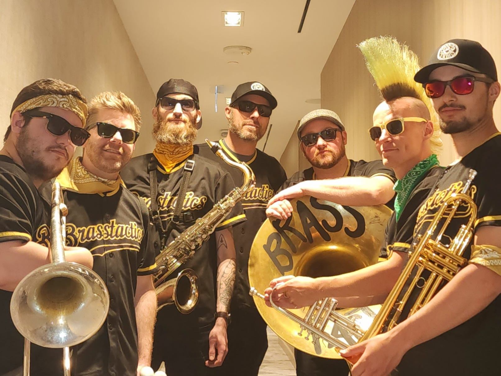 Brass band in matching jerseys and sunglasses holding trombone, saxophone, trumpet and sousaphone.