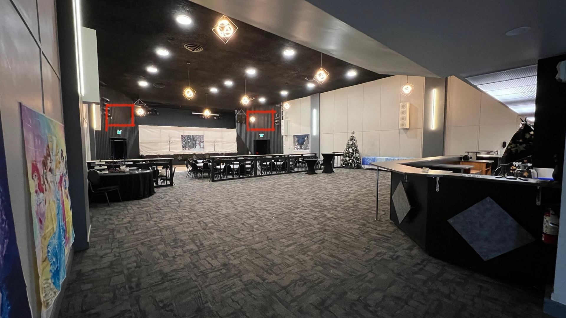 Event hall with tables, hanging lights, Christmas tree and princess posters on wall.