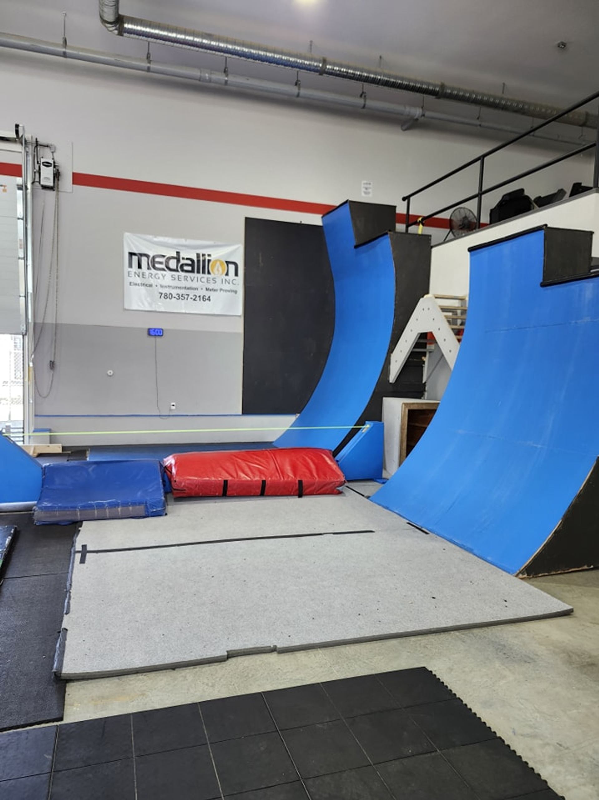 An indoor parkour or ninja warrior gym with blue and black obstacles, crash pads, and floor mats.