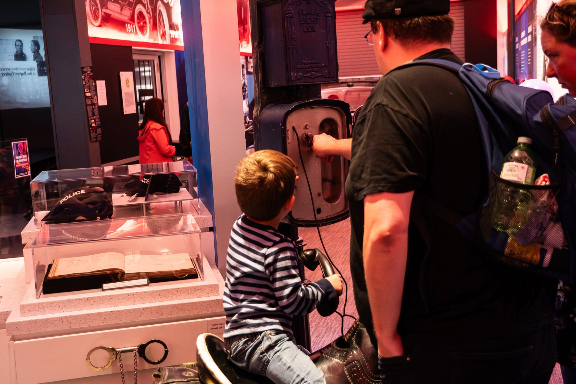 Museum visitors examine vintage police equipment display and interactive call box exhibit.