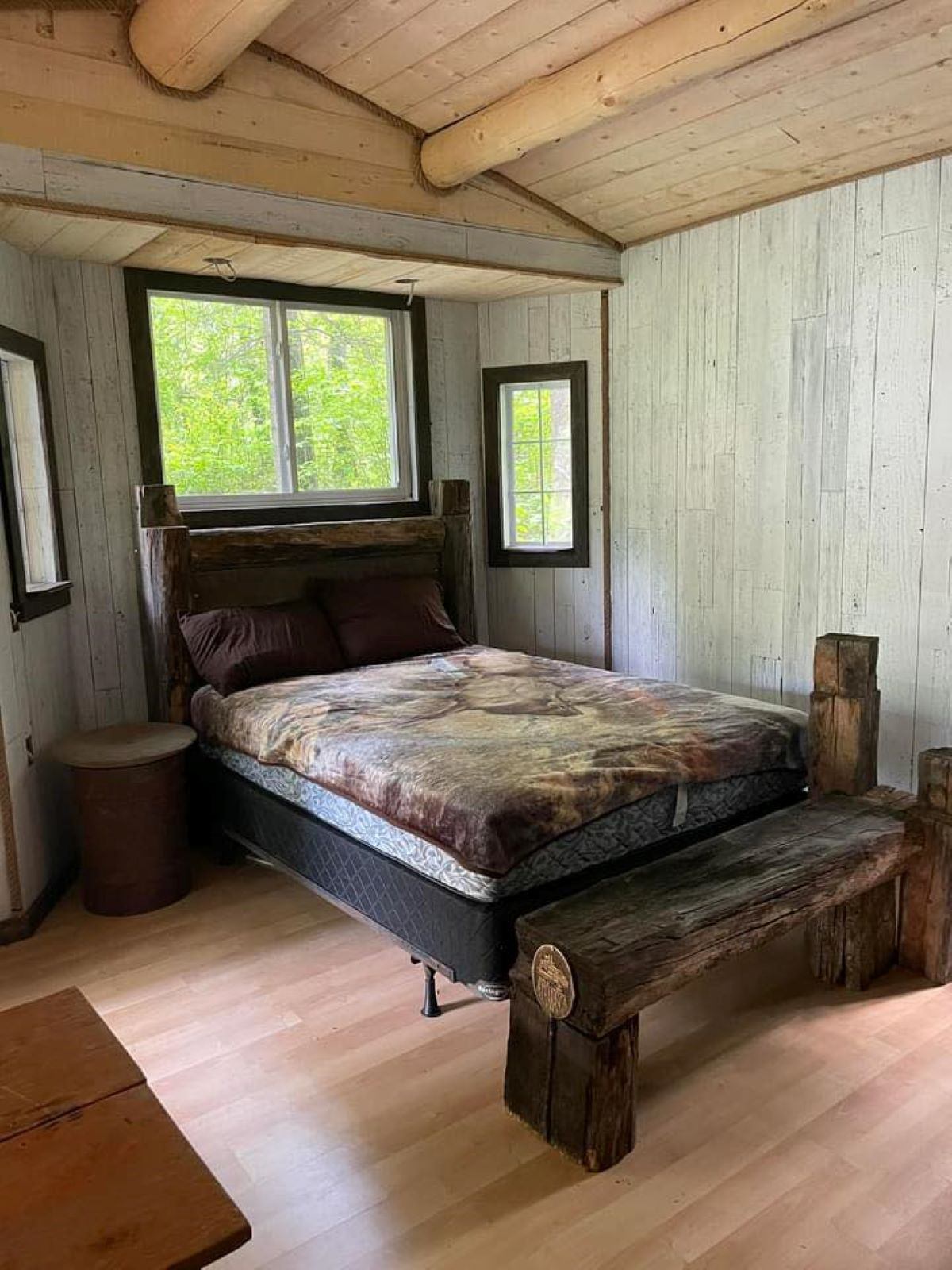 A log cabin bedroom with a wooden bed, natural wood walls, and large windows.