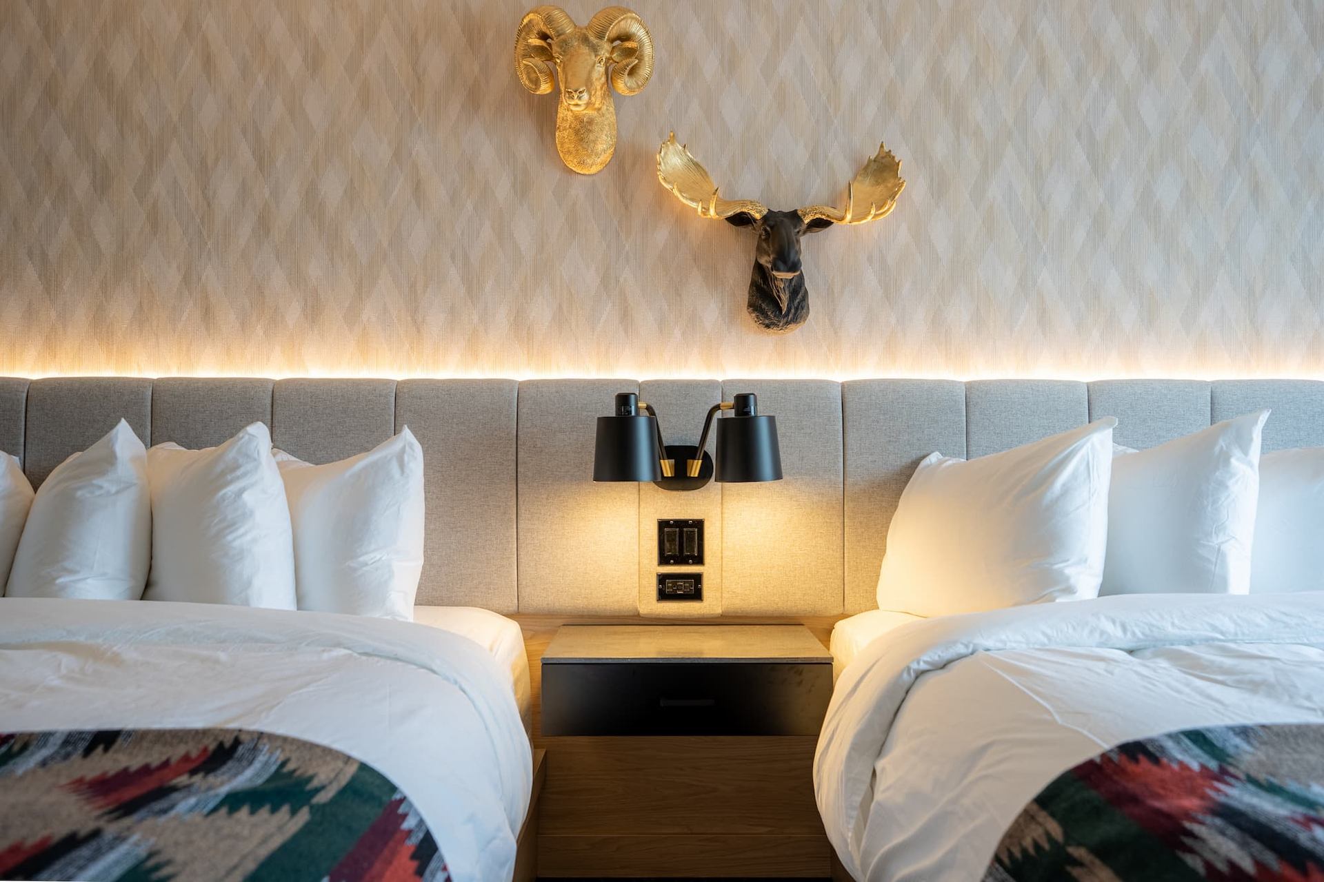 Cozy hotel room with two beds, warm lighting, and moose decor at Everwild Canmore.