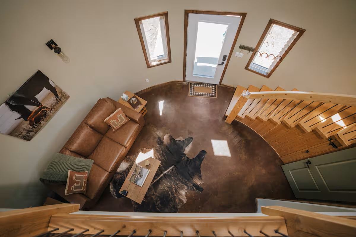 Saddle Hill Ranch cabin interior with leather sofa, cowhide rug, and wooden staircase.