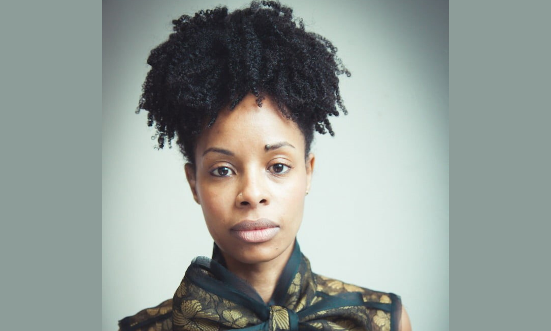 Portrait of a Black woman with natural curly hair, wearing a dark patterned top.