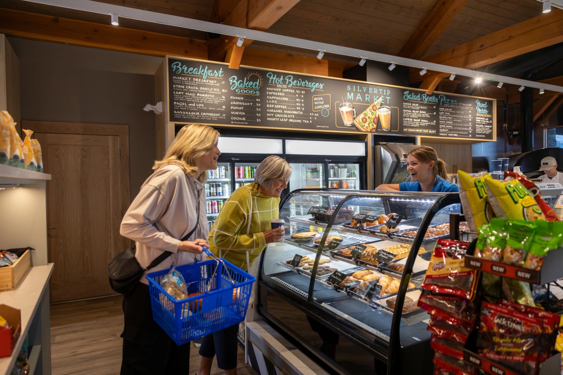 Customers browse pastries at Silvertip Market bakery counter beside refrigerated drinks.