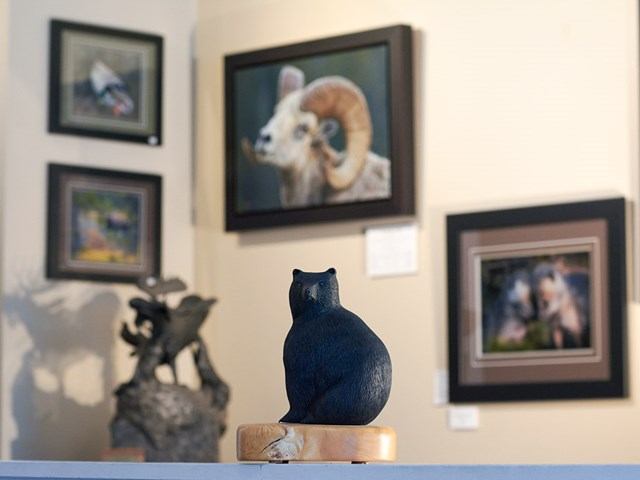 A carved bear sits in a gallery surrounded by wildlife paintings and sculptures of mountain animals.