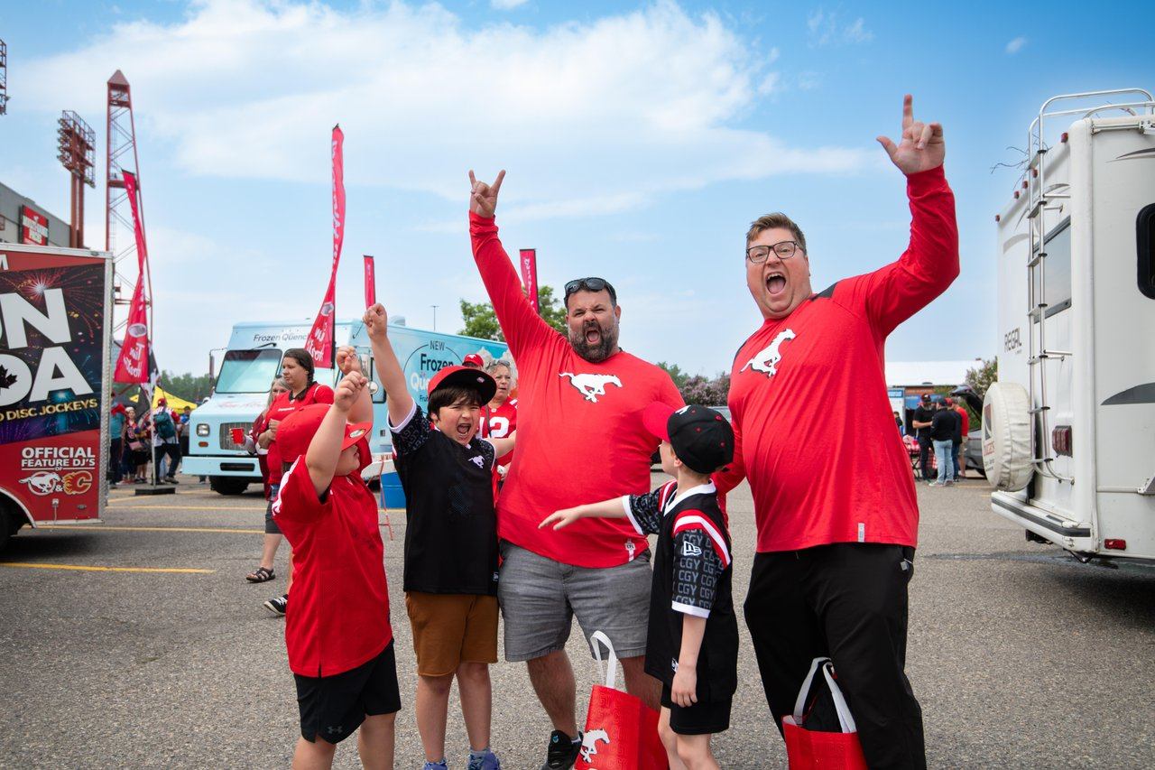 Calgary Stampeders fans raise their arms outside a stadium beside food trucks.