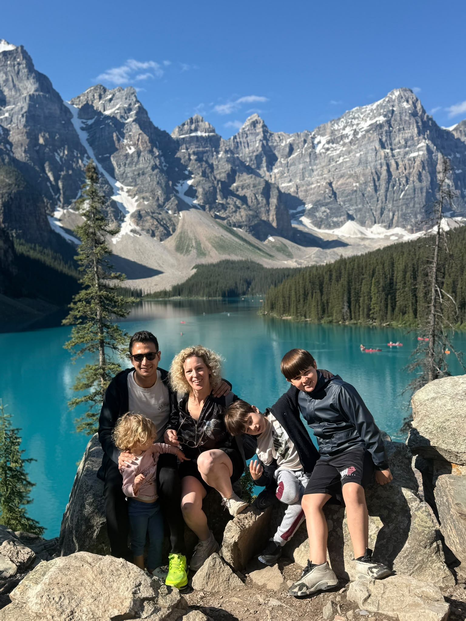 Group poses on rocks overlooking a turquoise mountain lake and snow-dappled peaks.