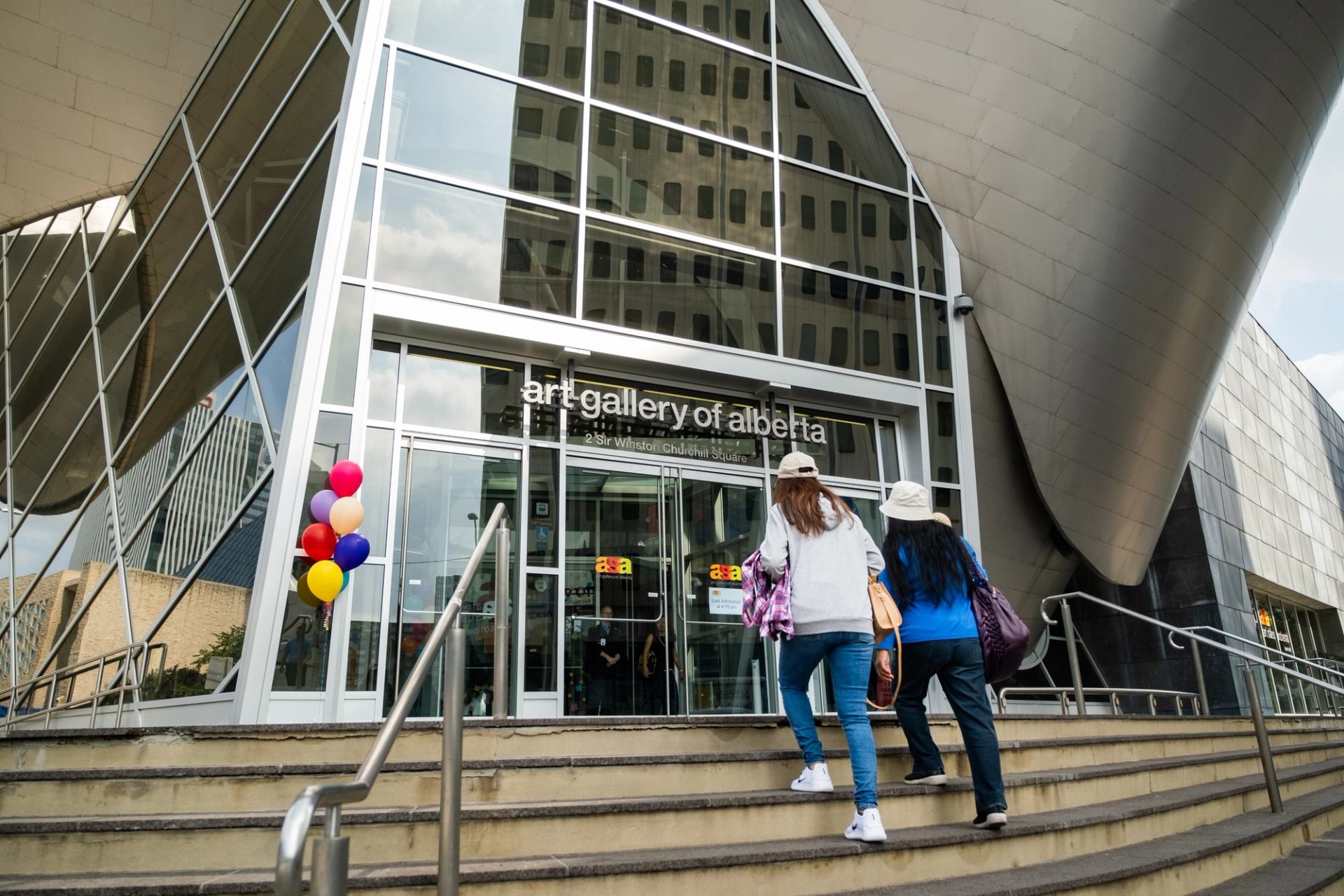 Visitors climb the steps toward the glass entrance of the Art Gallery of Alberta.