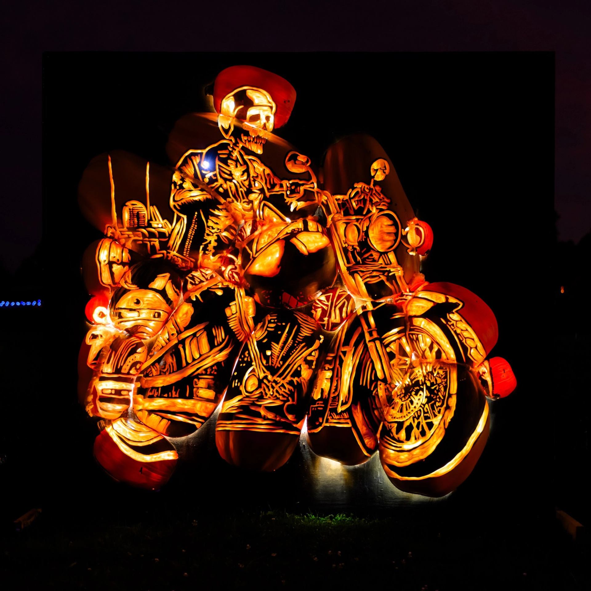 Pumpkins carved into a glowing skeleton on a motorcycle under dark skies
