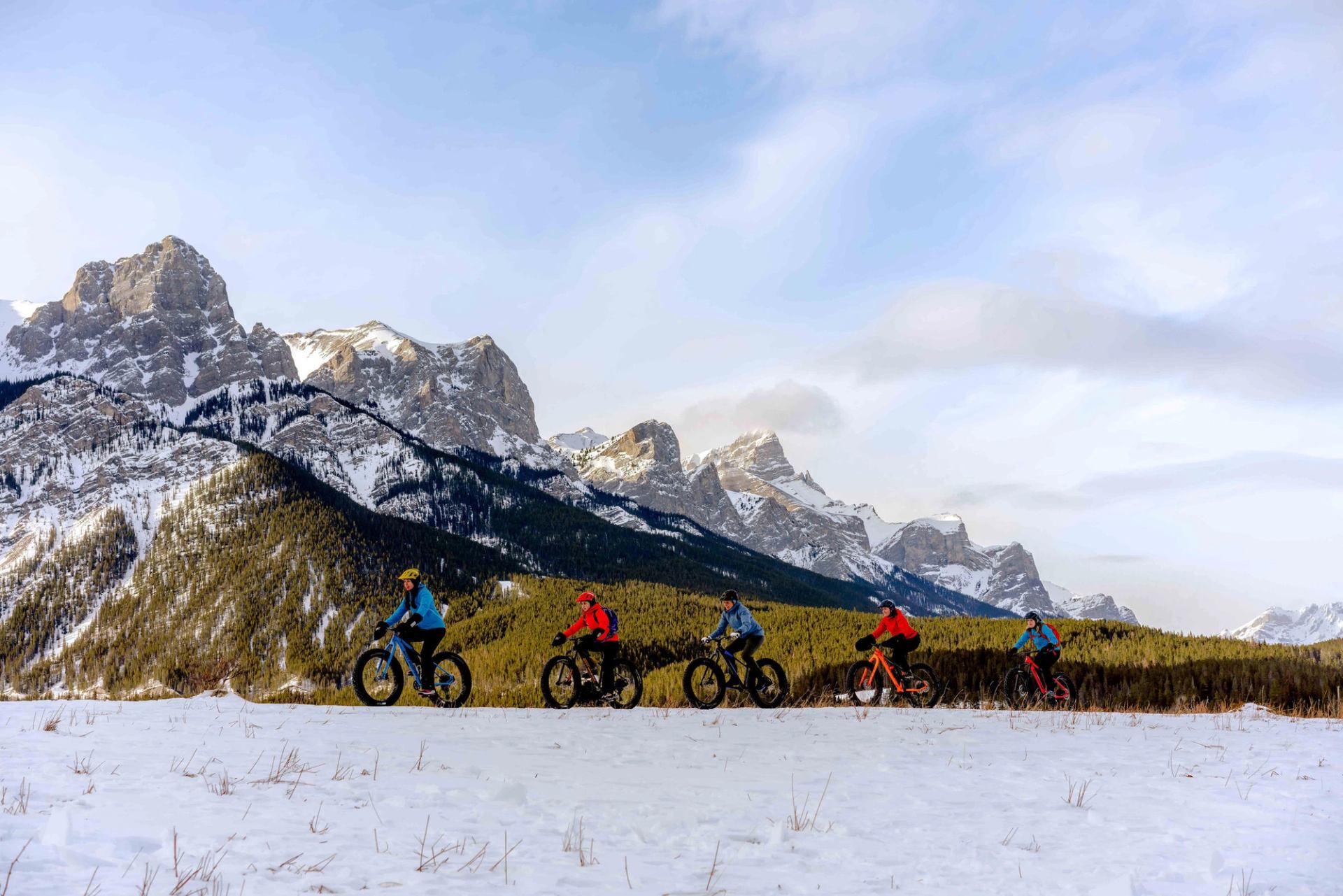 A group bikes single file on a fatbiking tour in Kananaskis Country, with mountains rising in the background.