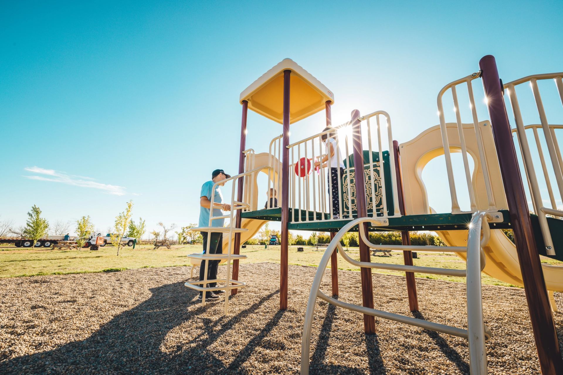 Playground with slides and climbing gear under clear blue sky, people enjoying the space.