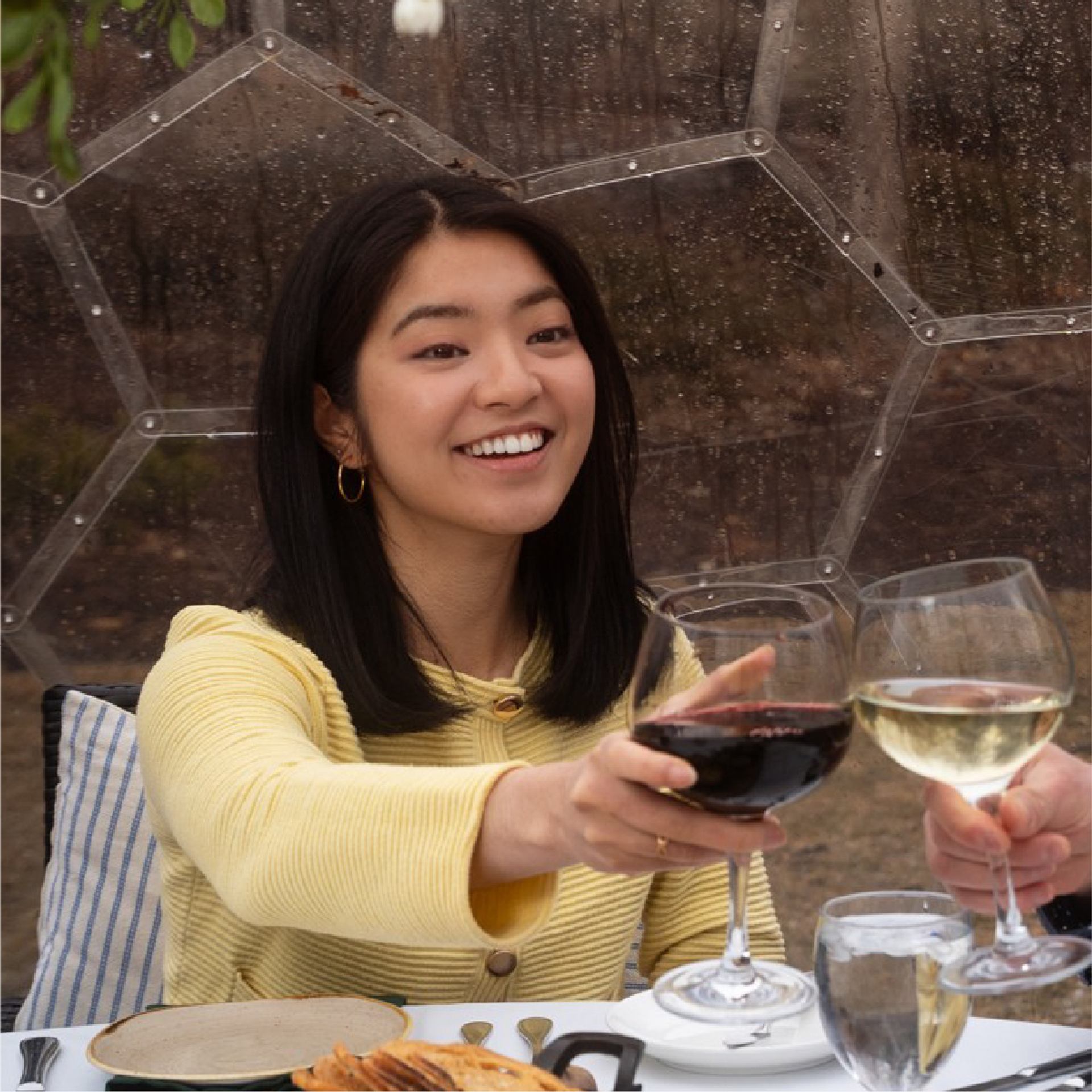 Smiling diner raises a glass of red wine toward another person's white wine.