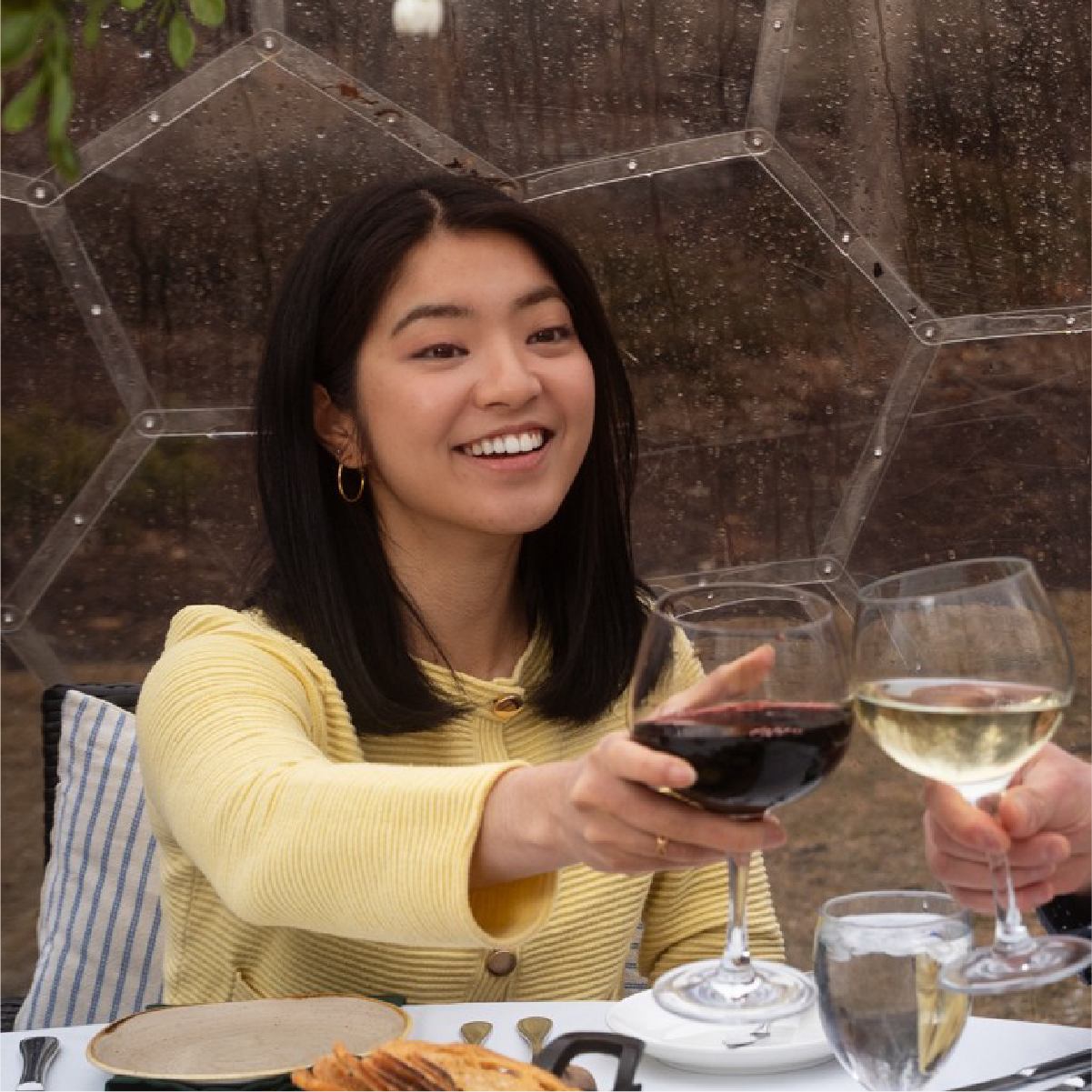 Smiling diner raises a glass of red wine toward another person's white wine.