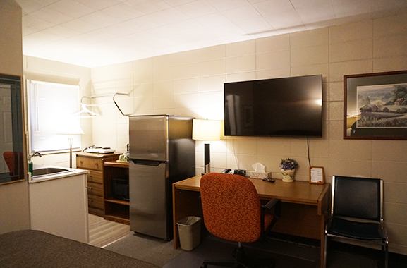 Motel room with desk, TV, mini fridge, and kitchenette area.
