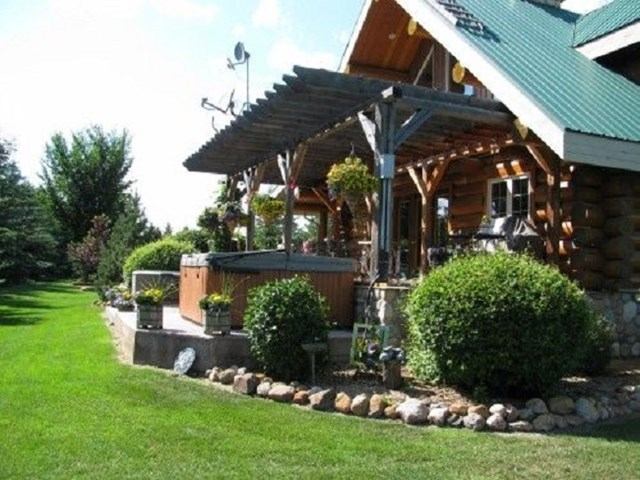 Log cabin with pergola, hot tub, and lush garden landscaping.
