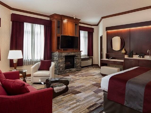 Hotel room with bed, stone fireplace, wall-mounted TV, armchairs and large window.