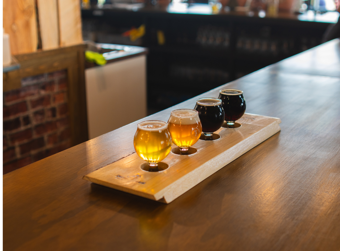 Beer flight with golden and dark samples rests on a wooden bar.