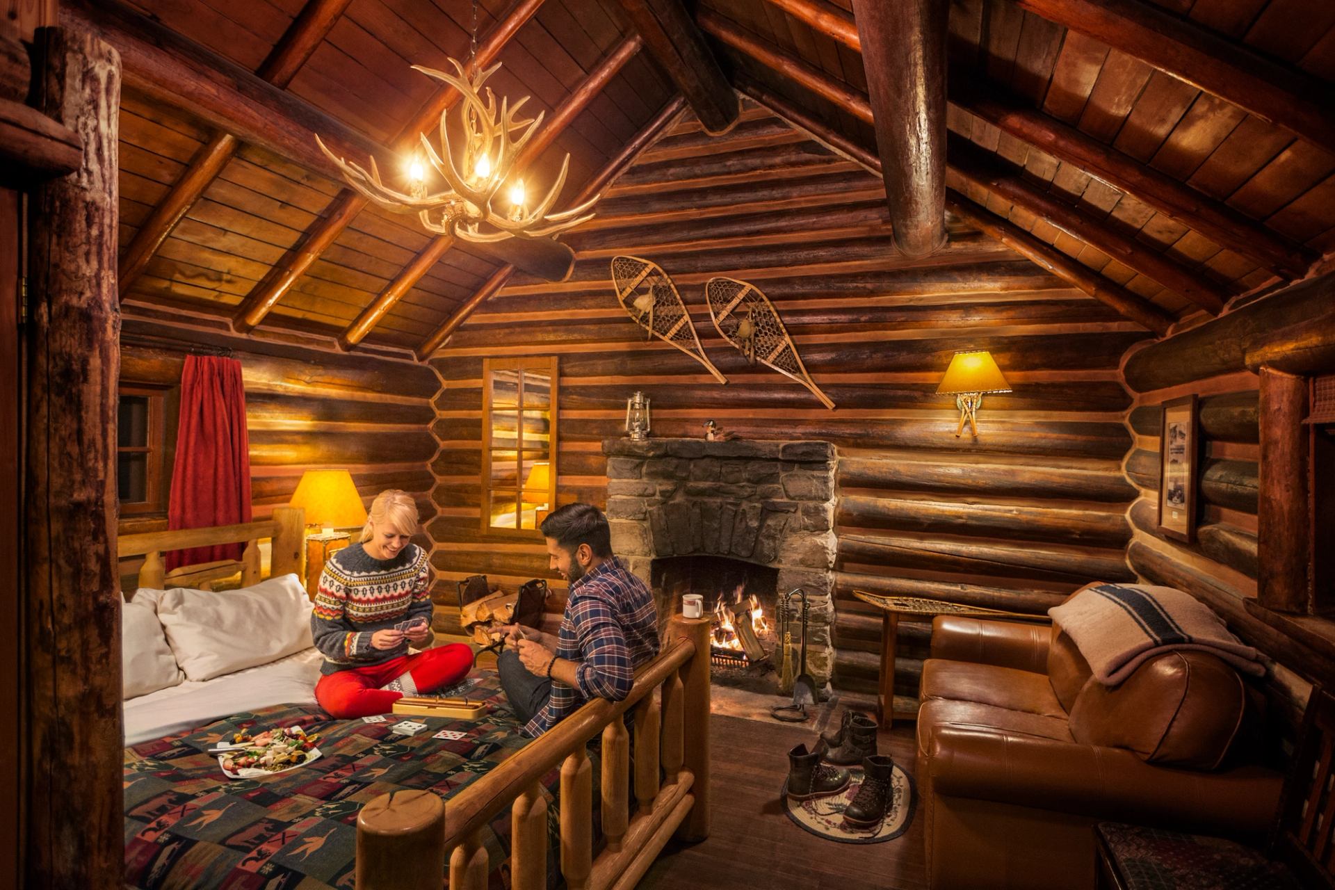 Two people relaxing by a fireplace in a cozy log cabin.