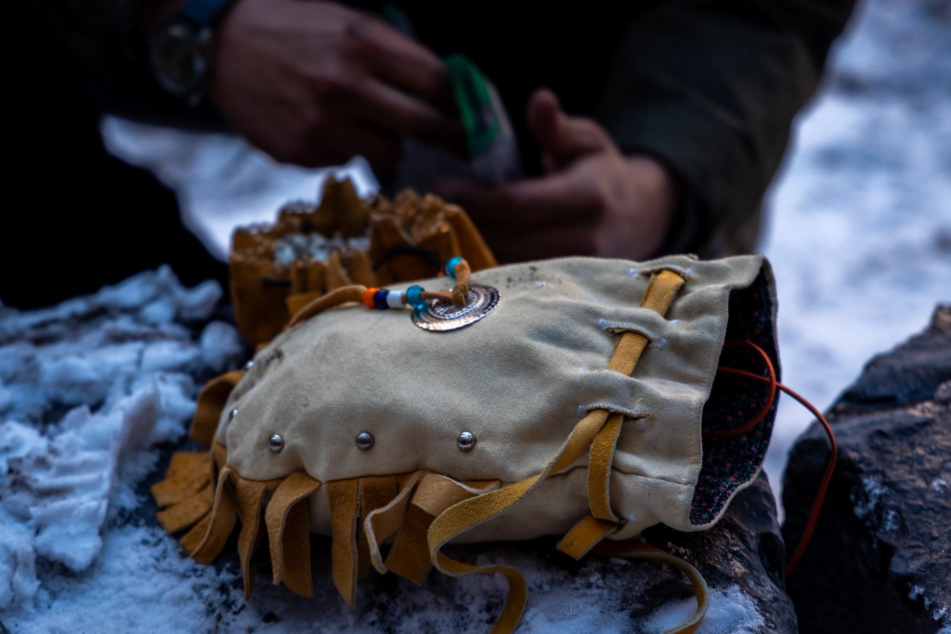 Beaded leather pouch with fringe rests on snowy rock, hands blurred in background.