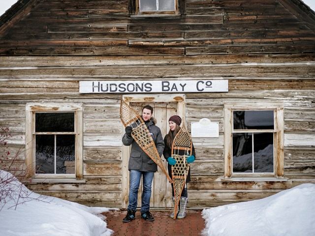People with snowshoes in front of historic Hudson’s Bay Co. building in snowy setting.
