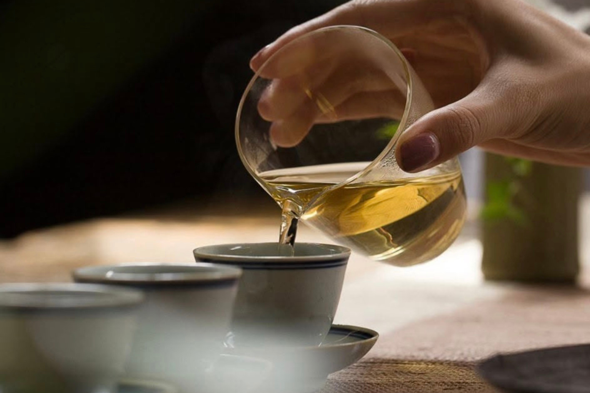 Hand pours tea from a glass pitcher into a ceramic cup.