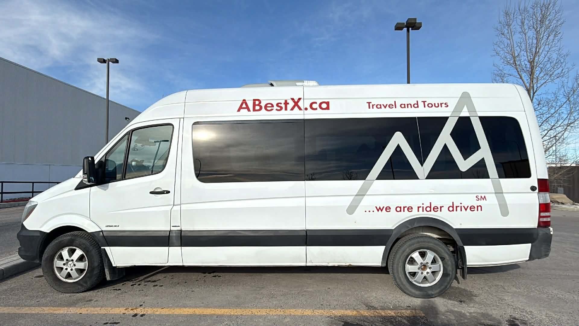 White ABestX.ca travel van with large window graphic parked in an outdoor lot.