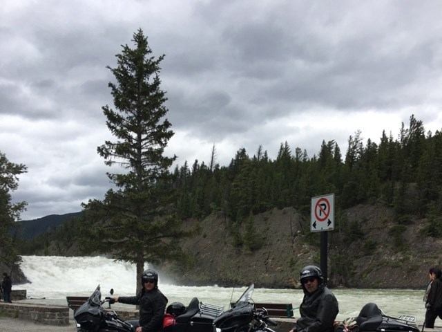 Motorcycles parked near waterfall in forested mountain area.