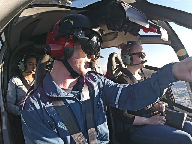 Interior view of a helicopter cockpit with pilot operating controls and passengers seated.