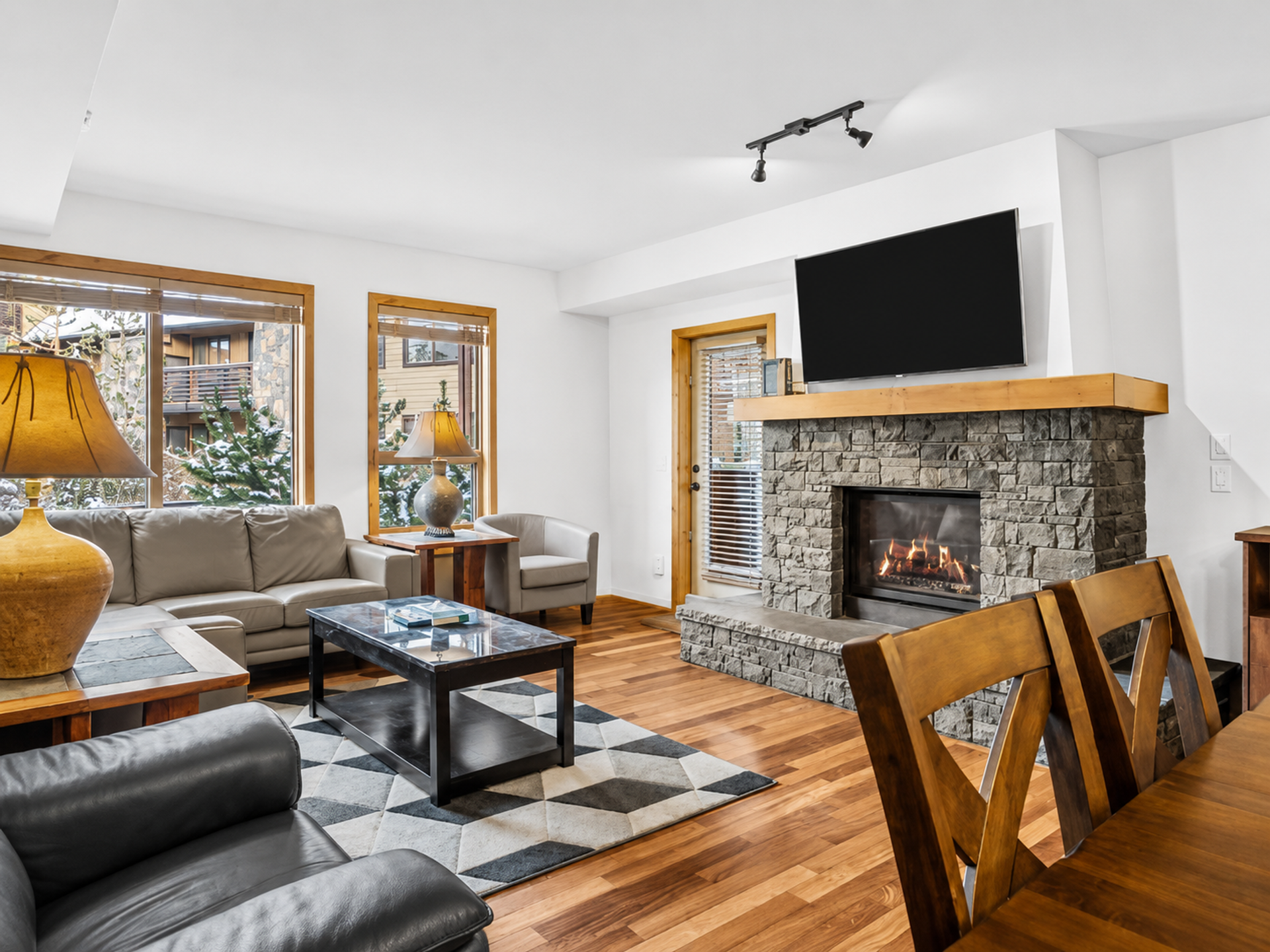 Living room with stone fireplace, leather sofas, large windows and wall-mounted television.
