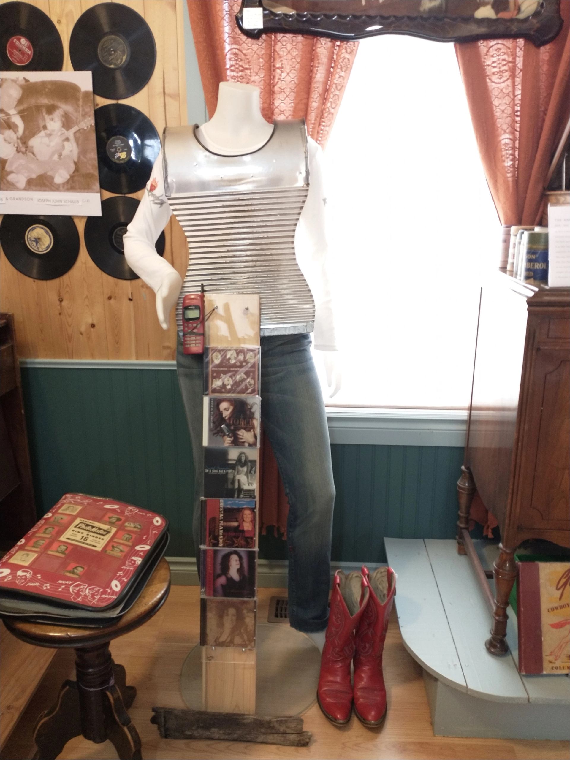 Mannequin wearing a white shirt in a museum display room with vinyl records and boots.