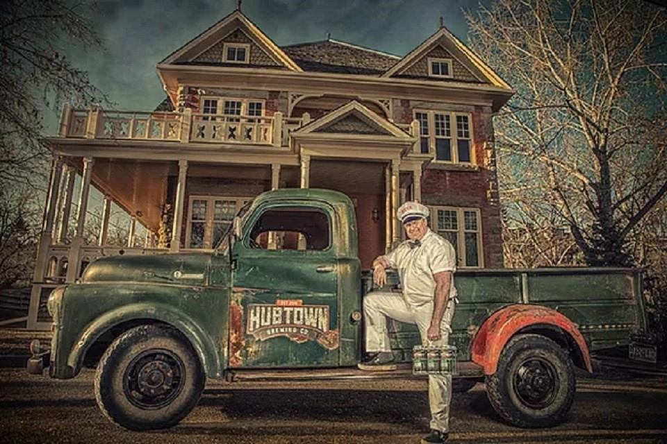 A man stood with his foot up on the running board of Hub Town Brewing antique pickup truck.