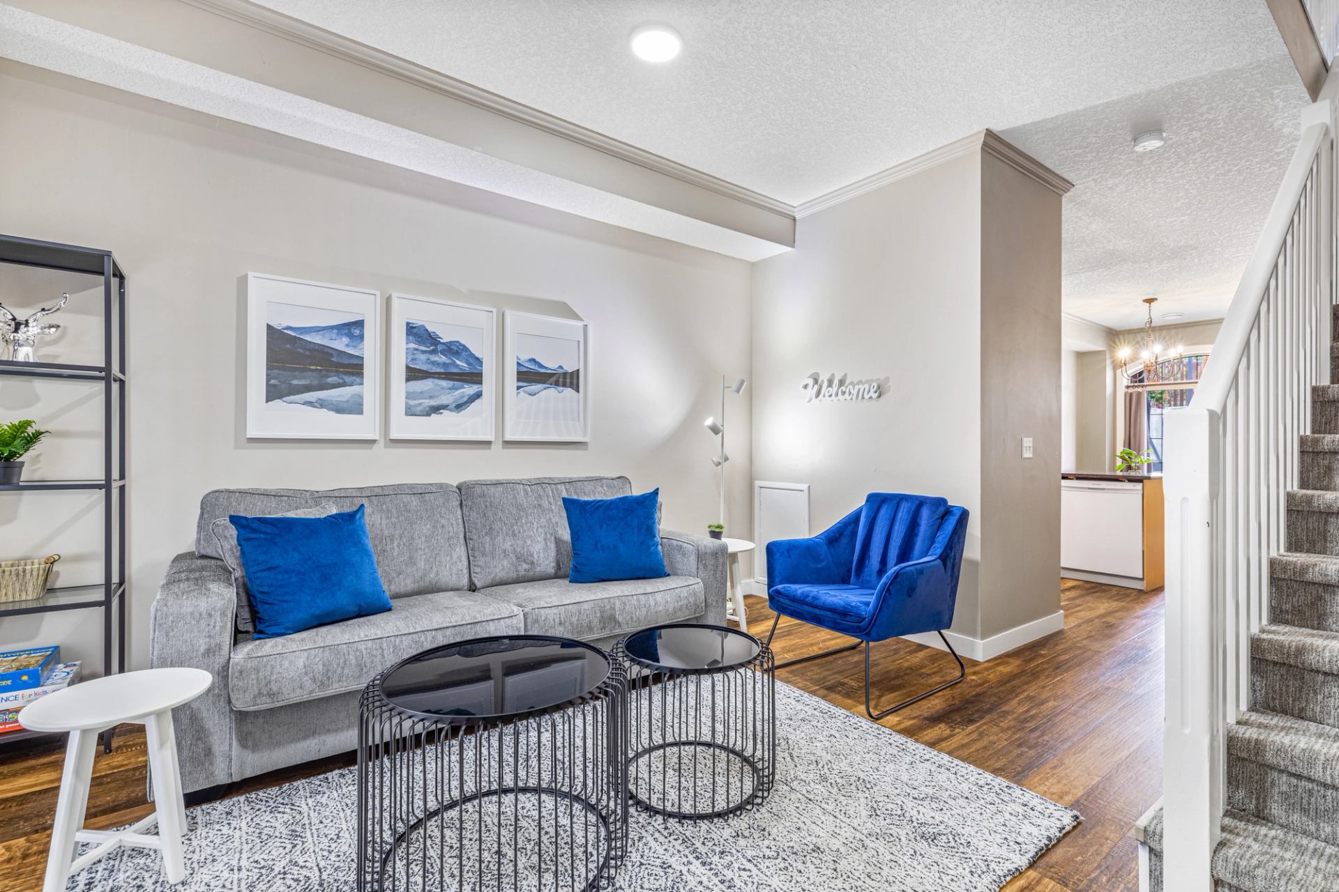 Living room with grey sofa, blue chair, nesting tables and carpeted staircase.