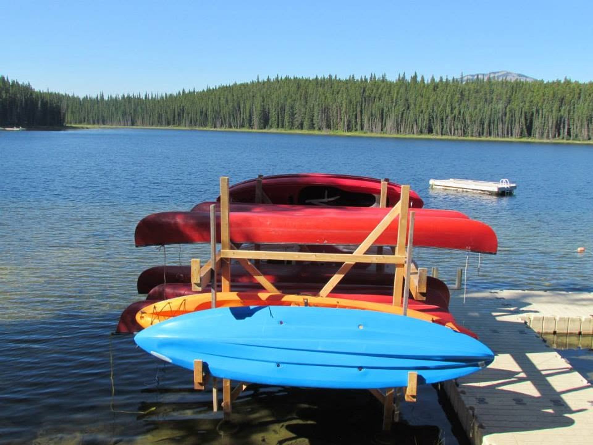 Stacked red canoes and a blue kayak on a dock beside a forested lake.