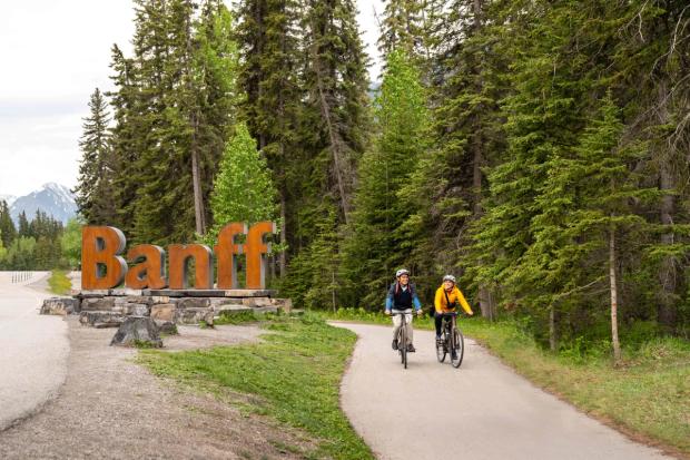 People riding bikes on path next to "Banff" sign.