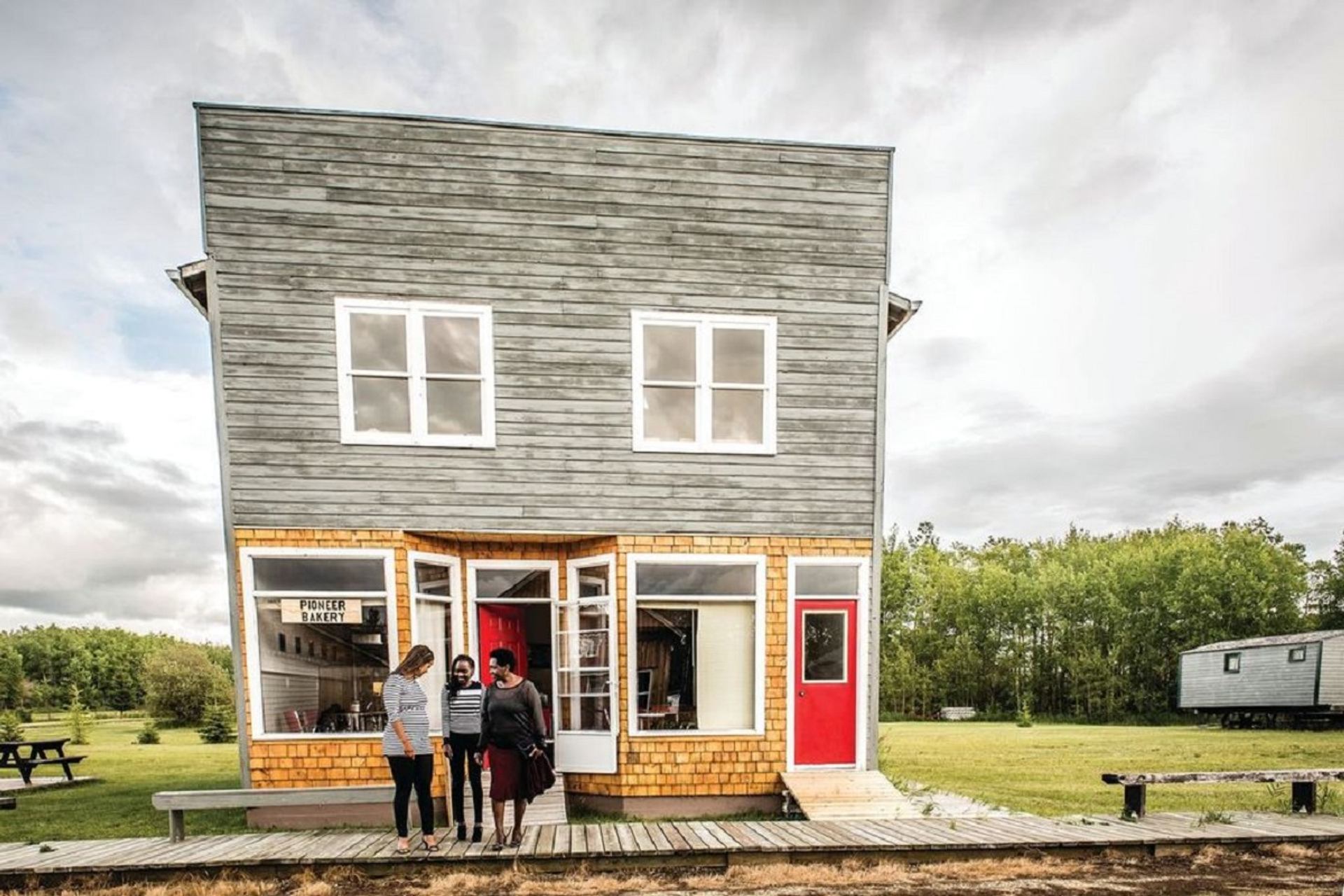 Historic wooden storefront with visitors standing on a boardwalk at Pioneer Village.