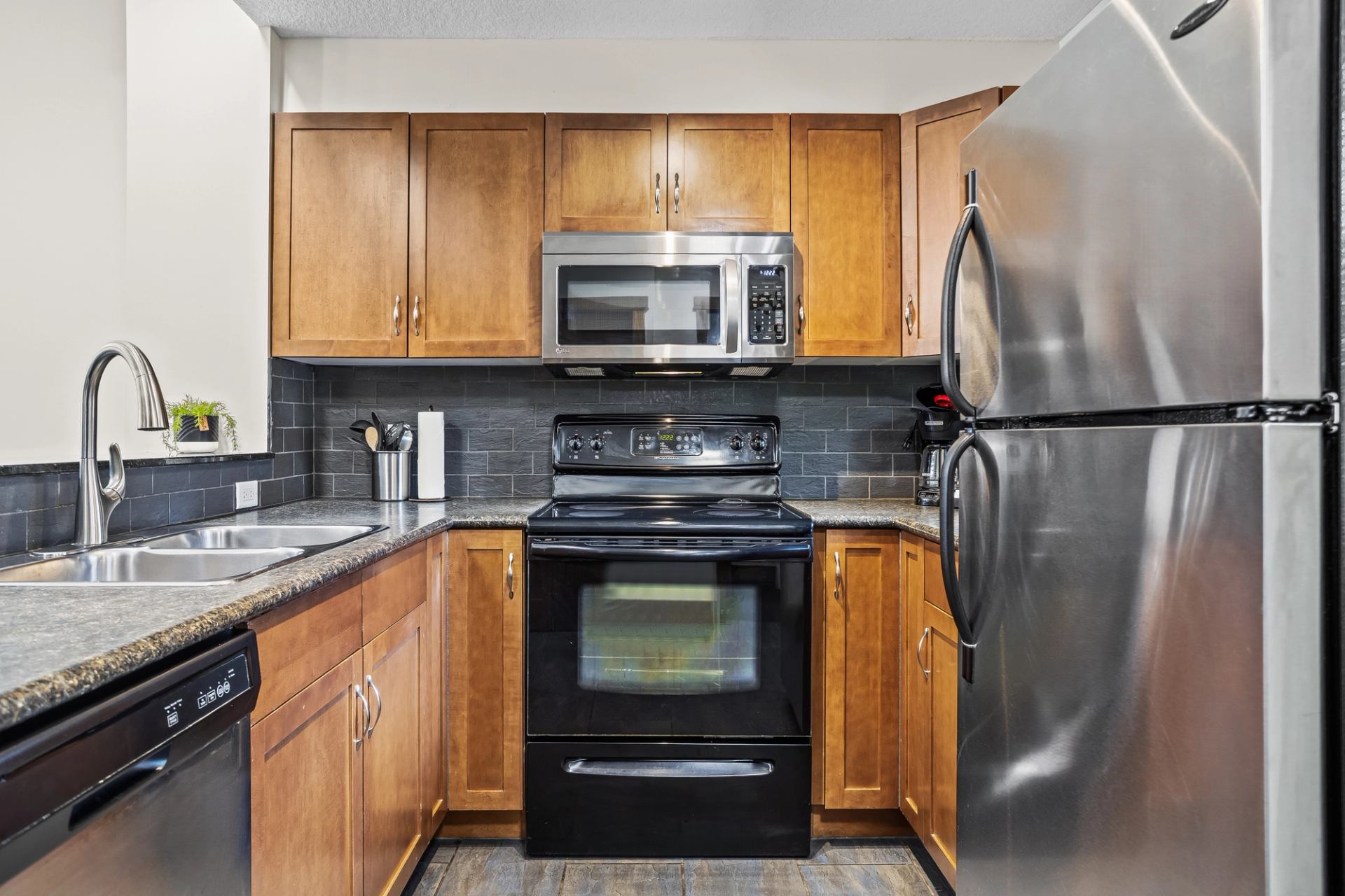 Kitchen with wood cabinets, stainless steel appliances, black stove and double sink.